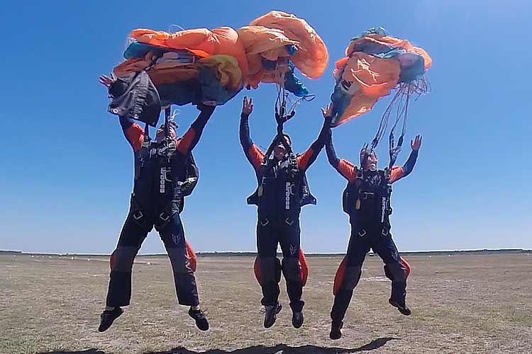 Drie skydivers maken een gezamenlijke landing tijdens een skydivevakantie bij Airboss, onder kleurrijke parachutes op een zonnige dag.