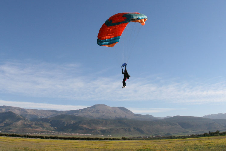 Skydiver landt met kleurige parachute bij Beni Mellal; Atlasgebergte op de achtergrond.