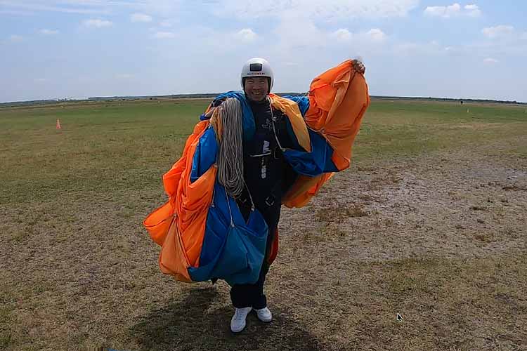 Student after a first skydive, smiling widely with parachute after landing